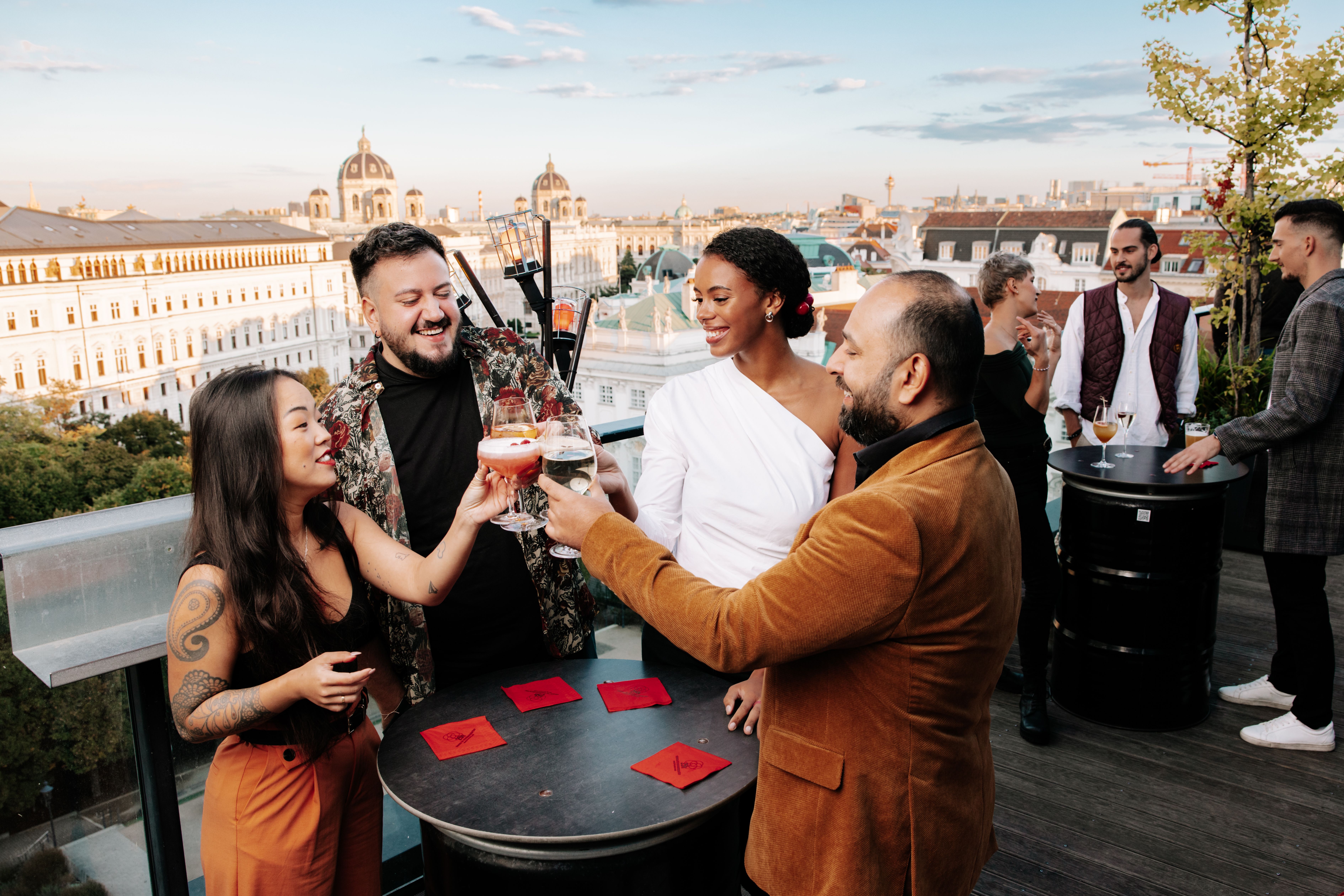 Foto: Ansicht von mehreren fröhlichen Menschen die mit Gläsern anstoßen in der dachboden - Rooftop Bar am 25hours Hotel beim Museums Quartier
