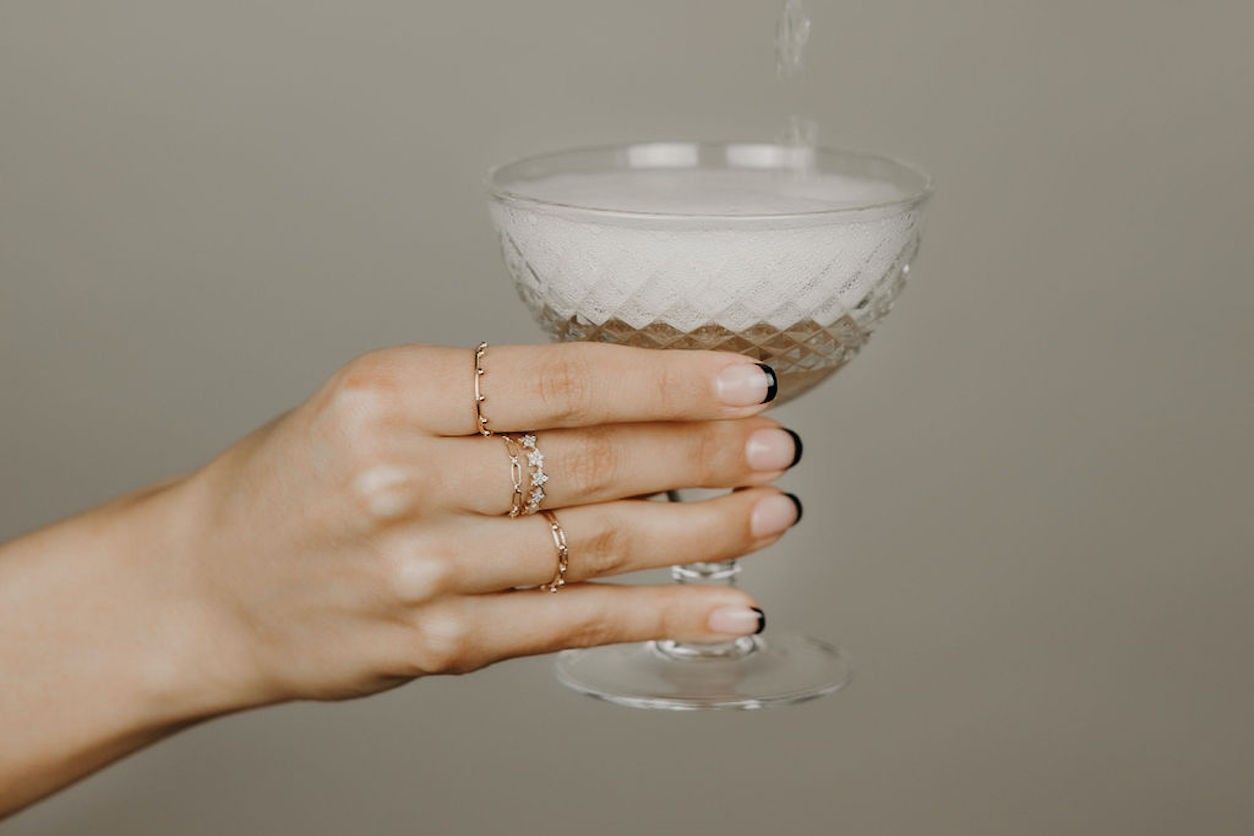 Foto: Eine Frauenhand mit Ringen hält ein Champagnerglas mit Champagner.