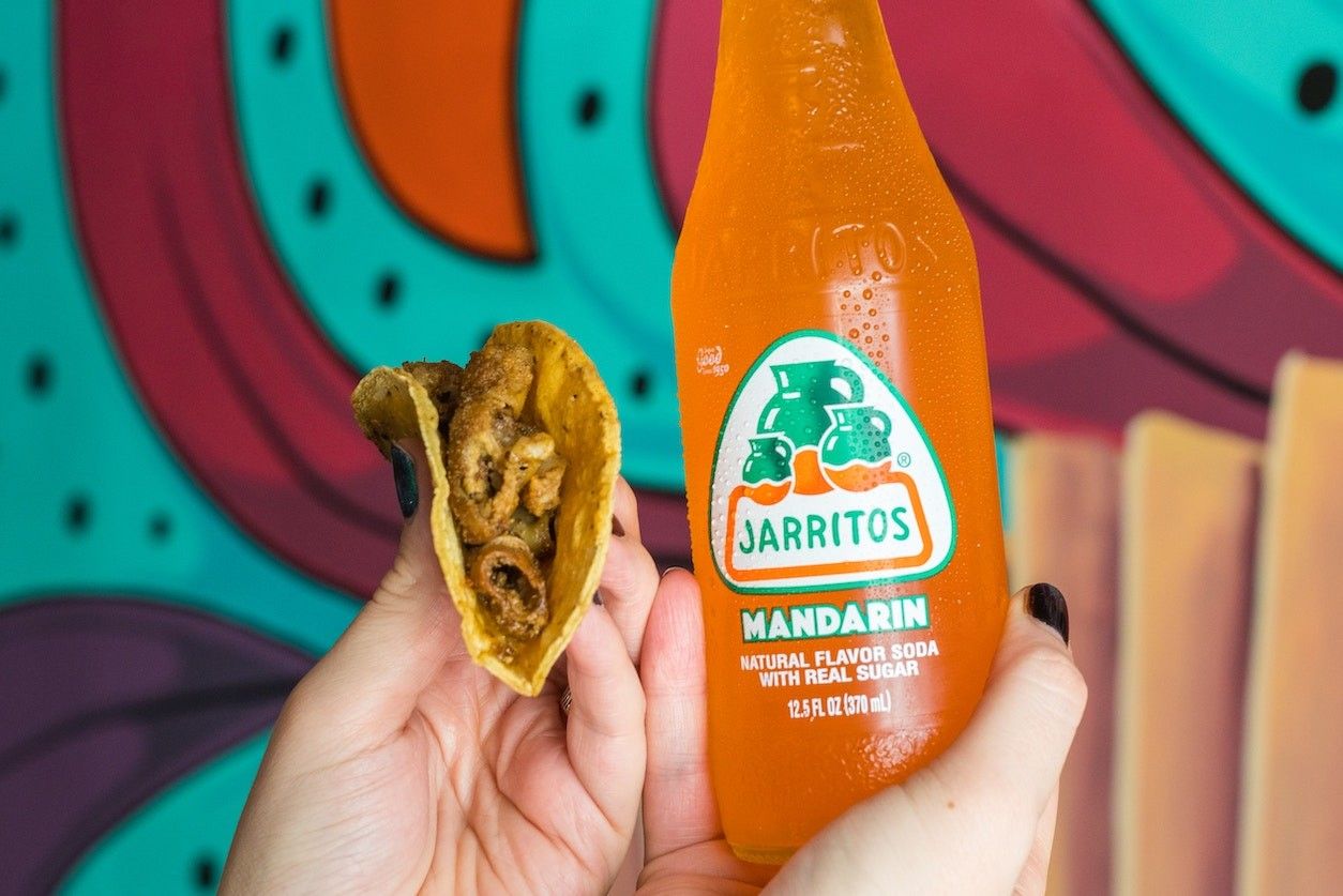 Foto: Ein Burrito und ein Mandarinengetränk gehalten von zwei Händen.