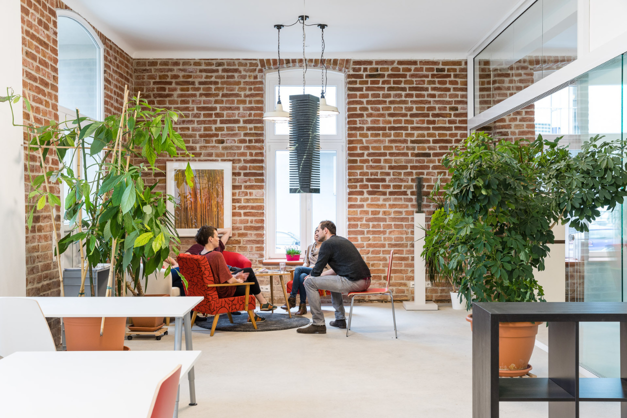 Foto: Raum mit Tischen, Pflanzen und Menschen die an einem kleinen Tisch zusammensitzen
