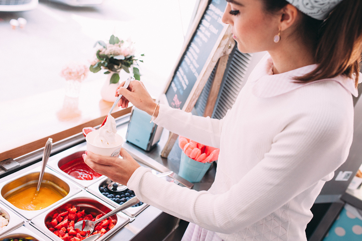 Foto: Eine Frau macht gerade ein Frozen Joghurt. Verschiedene Früchte und Saucen.
