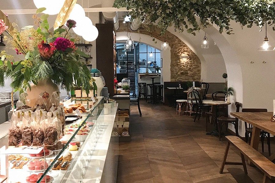 Foto: Innenraum einer Bäckerei mit Tischen, Sesseln und Bänken sowie eine Theke mit französischen Süßigkeiten.
