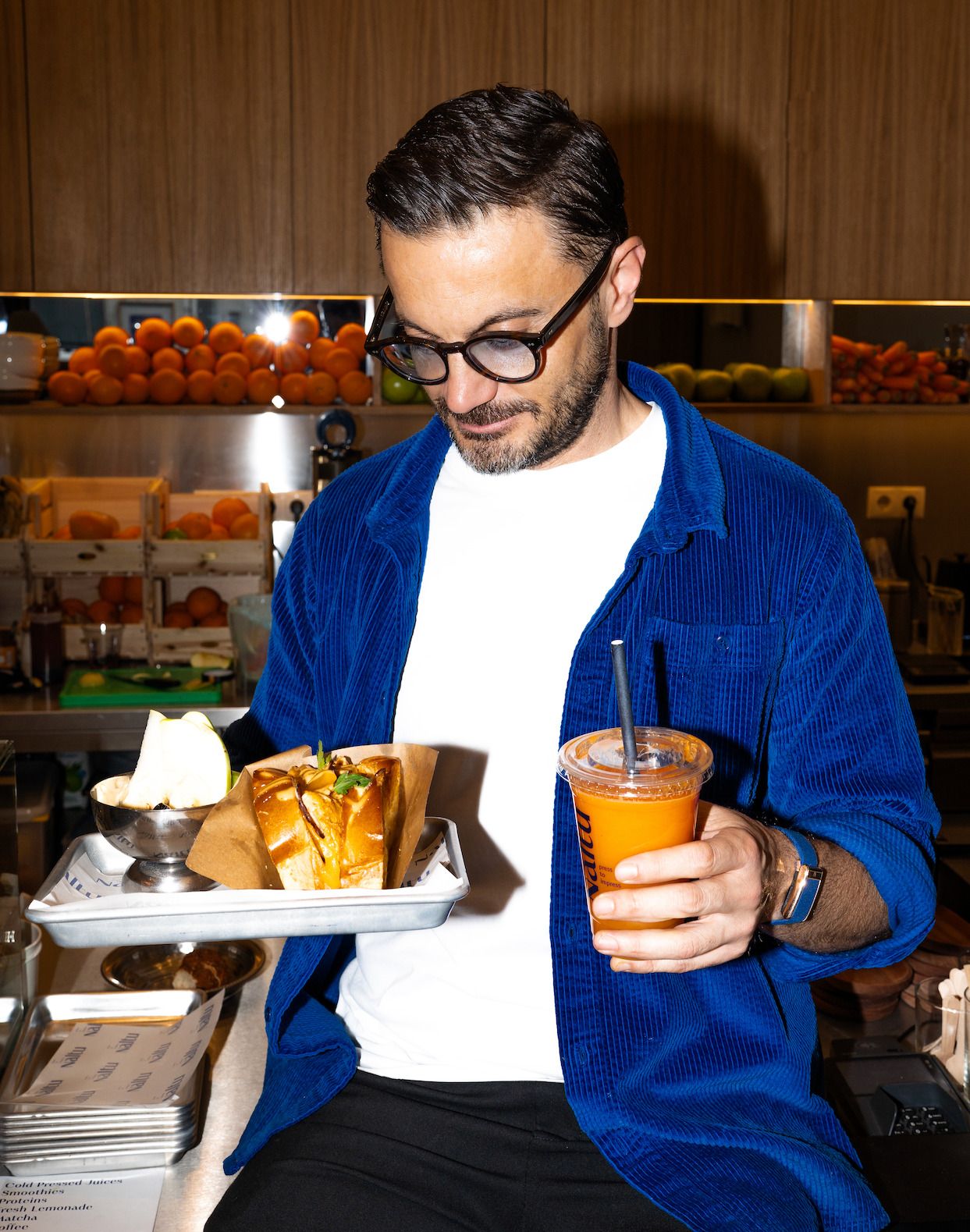 Foto: ein Mann mit Brille und blauem Hemd hält ein Tablett mit einem gutbelegtem Brot und in der anedern Hand einen Shake