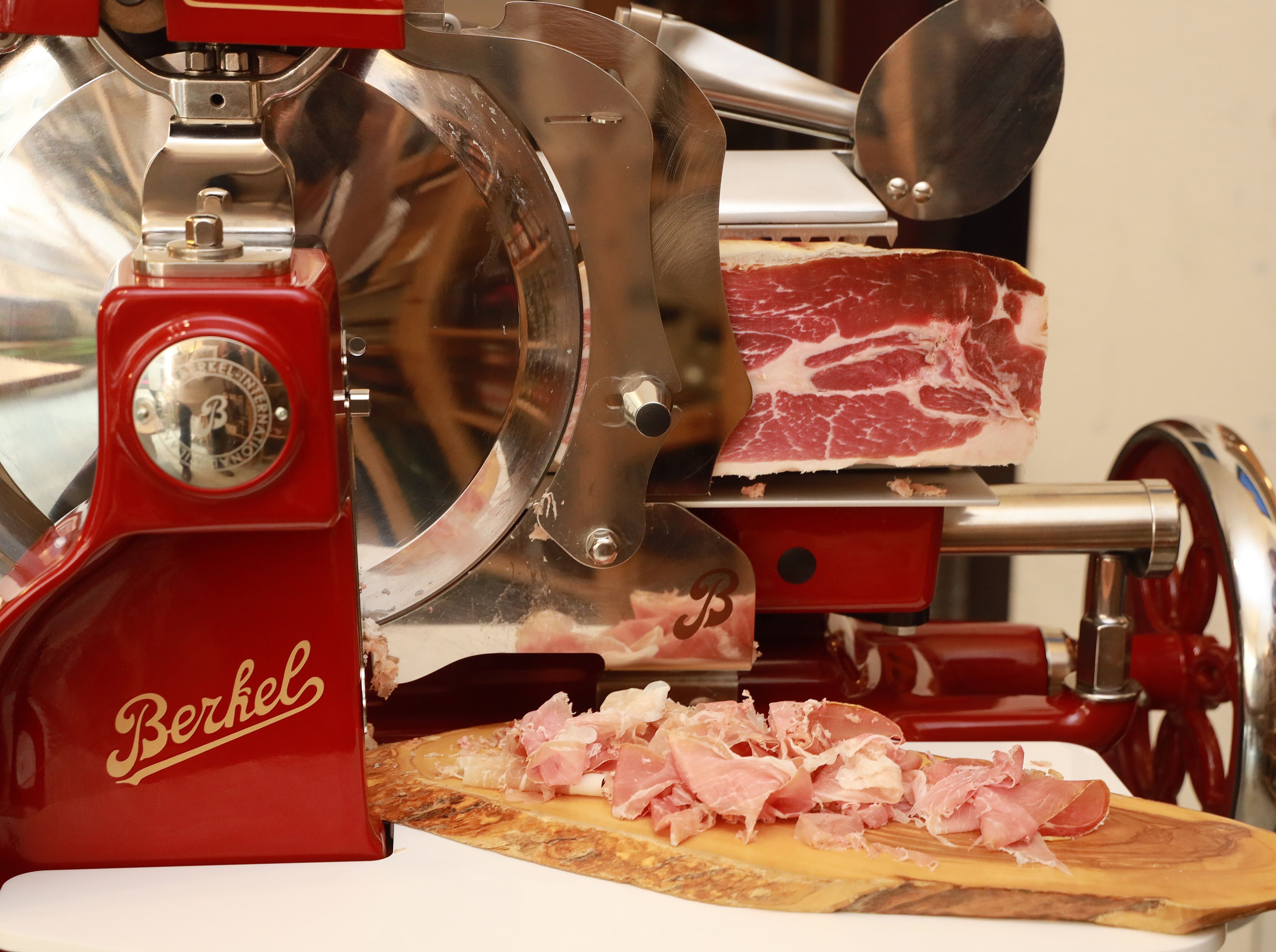 Foto: Ansicht einer roten Schneidemaschine für Prosciutto. Zu Sehen ist appetitlich aufgeschnittener Prosciutto