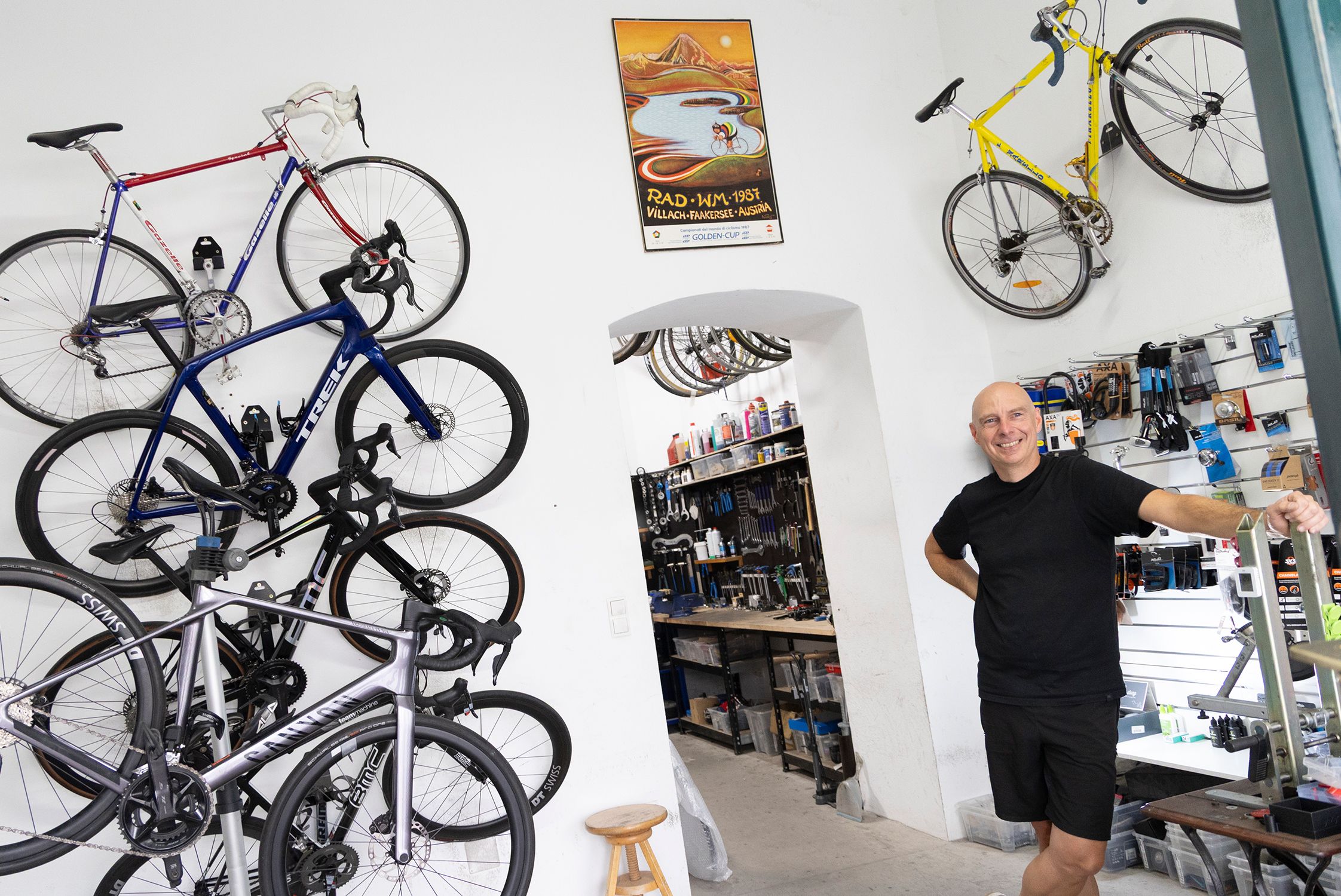 Foto: Innenansicht der Fahrradwerkstatt. Ander Wand hängen Fahrräder, der Besitzer lächelt freundlich
