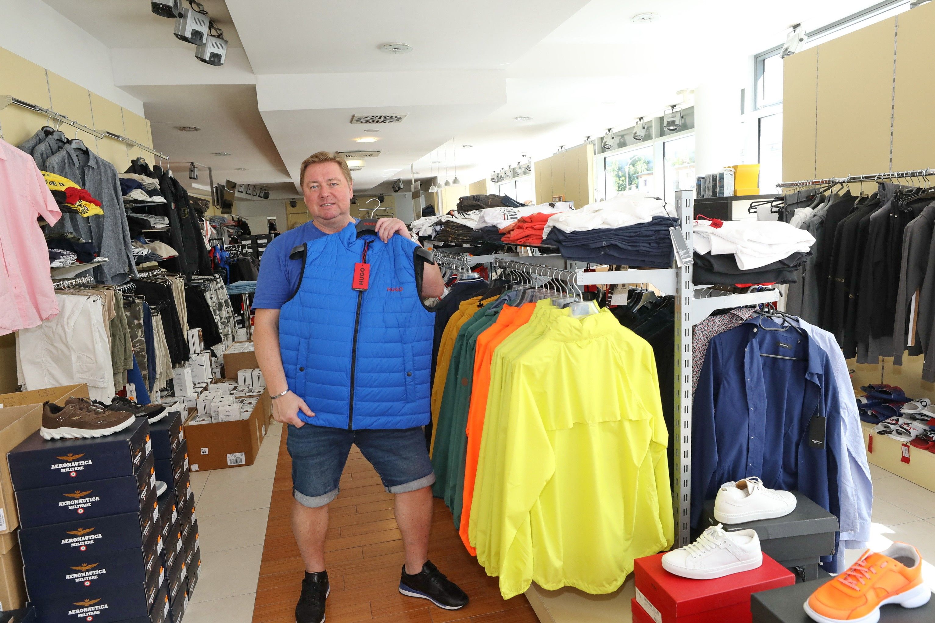 Foto: Verkaufsraum von ADAMS MODEN mit unterschiedlichen Jacken und Mann, der ein Gelee hochhält und zeigt