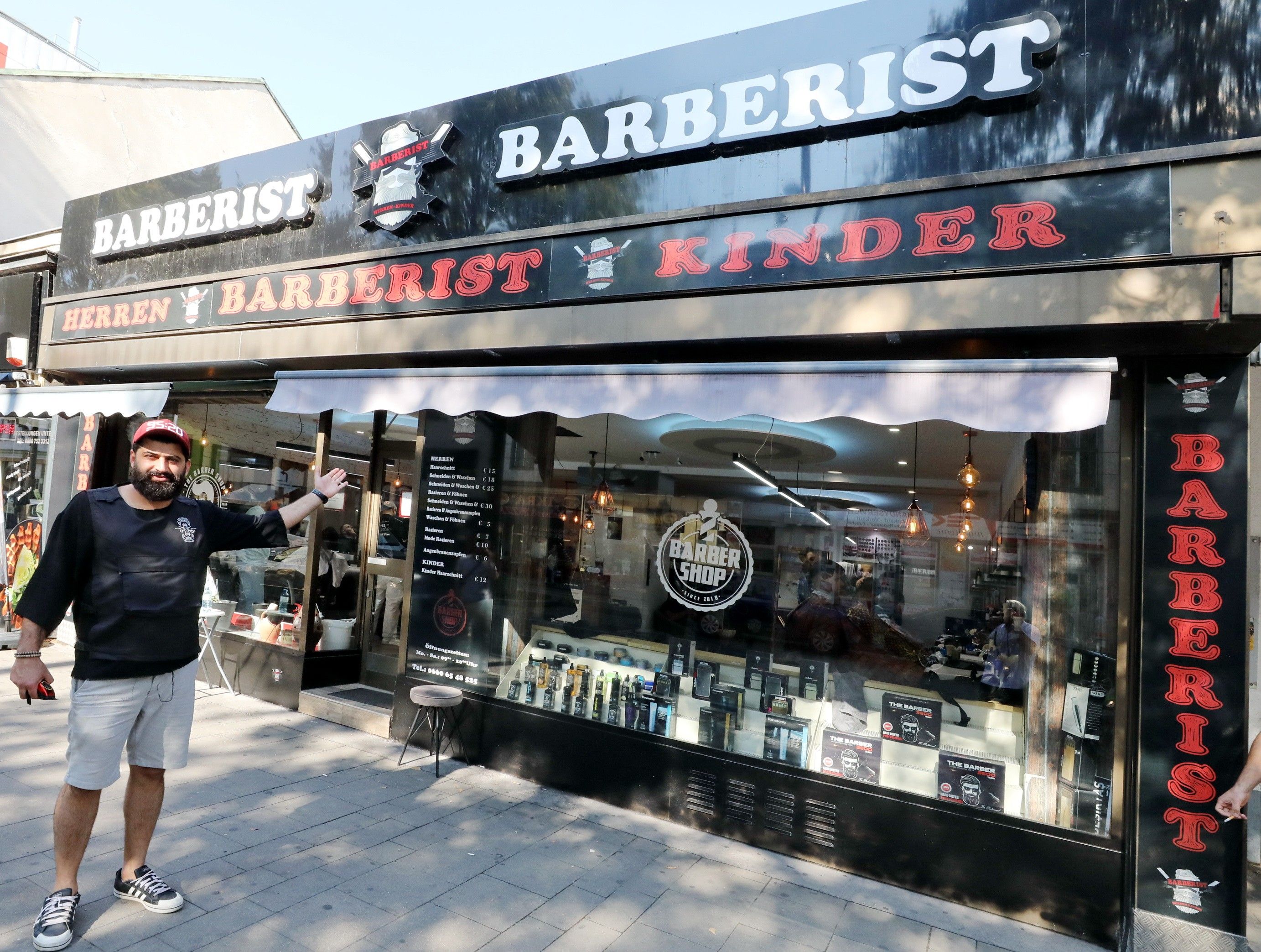 Foto: Eingangsbereich des Barberist Friserusalons mit Mann der der auf die Auslange des Salons zeigt
