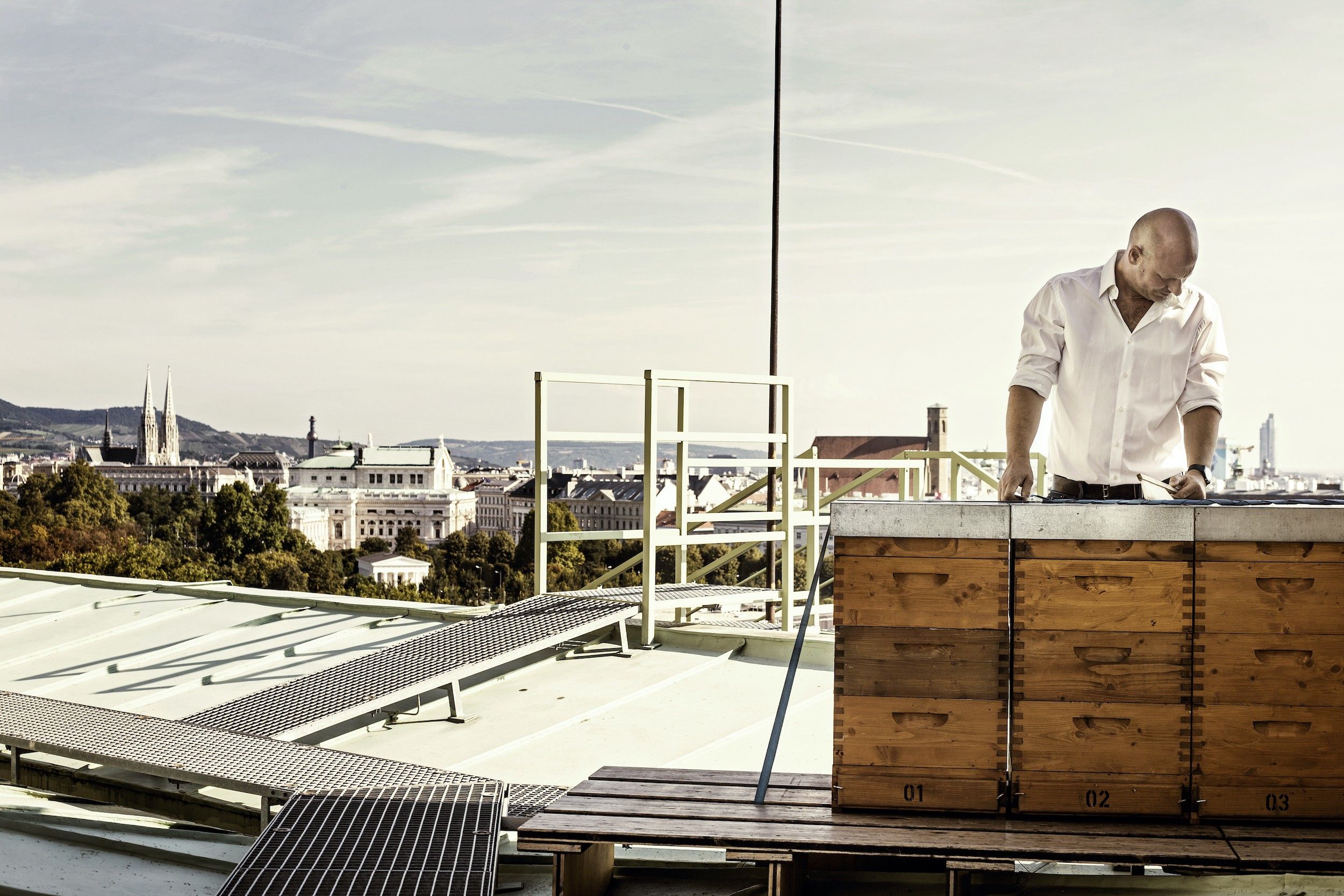 Foto: Am Dach stehen Bienenstöcke und ein Mann lehnt daran