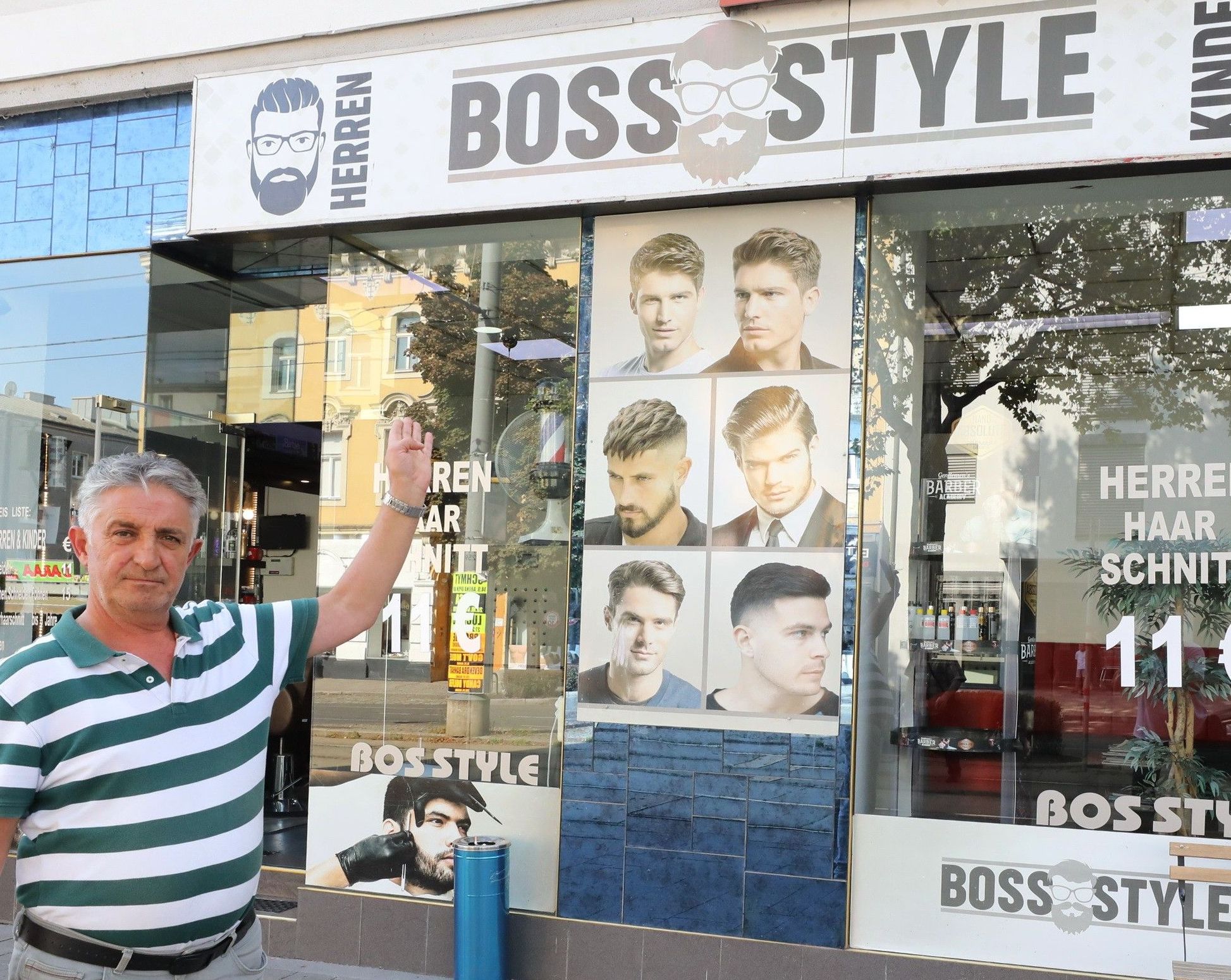 Foto: Eingangsbereich von Boss Style, ein Mann zeigt auf die Auslage auf der verschiedene Haarschnitt-Model-Bilder zu sehen sind.