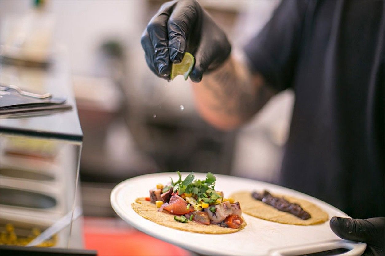 Foto: Eine Person hat ein Gericht in der Hand und träufelt eine Zitrone darüber.