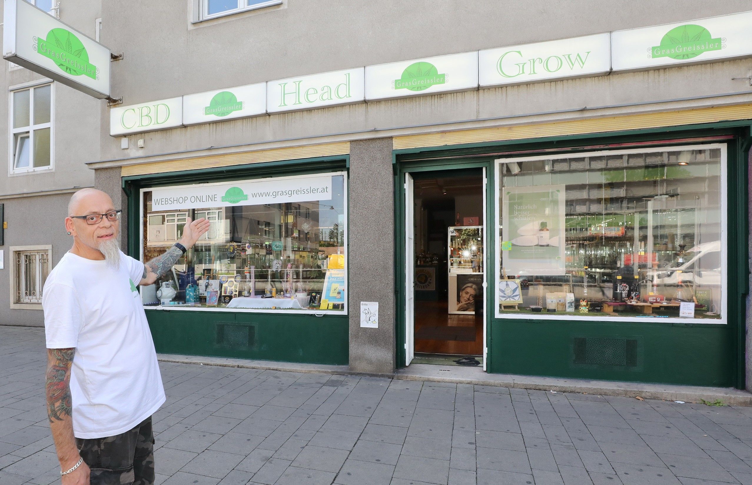 Foto: Auslage des Gras Greisslers und Mann, der auf den Eingang zeigt