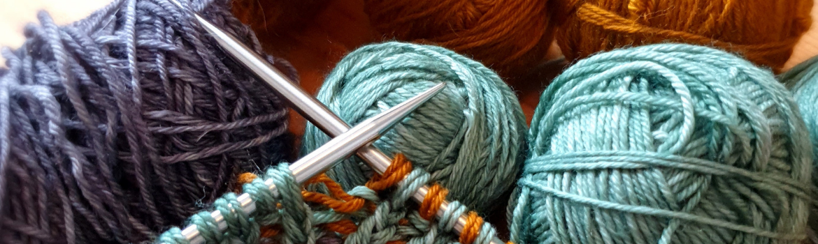 Foto: Verschiedene Wollknäuel und zwei Stricknadeln