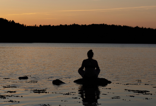 Foto: Eine Person sitzt auf einem Stein im Wasser und meditiert
