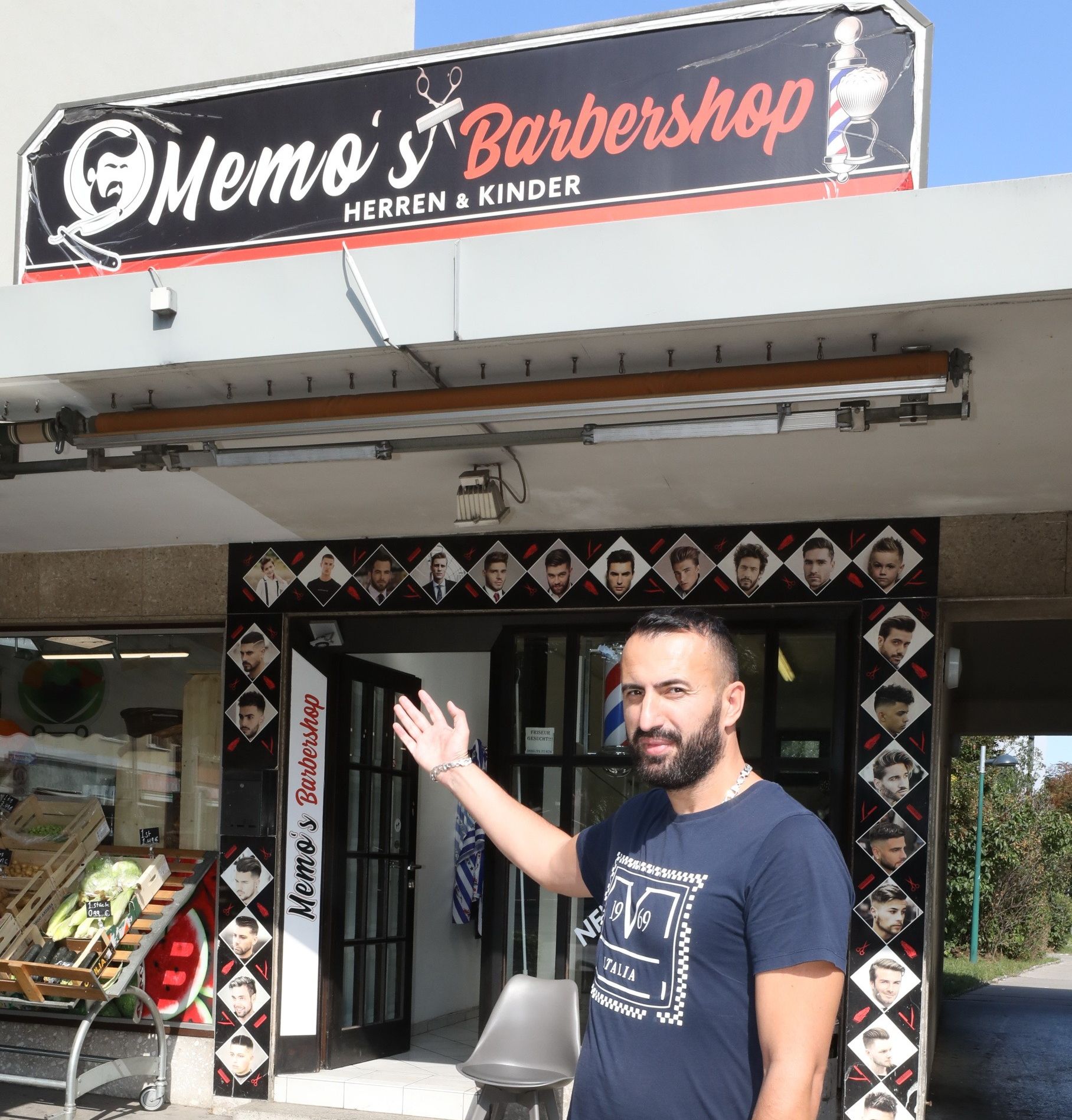Foto: Eingangsbereich von Memo's Barbershop vor dem ein Mann auf den Eingang zeigt, der mit unterschiedlichen Modelbildern umrandet ist