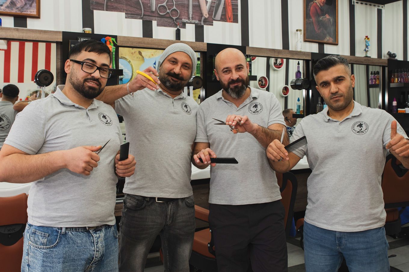 Foto: Innenansicht des barbershops mit vier Personen mit gebrandeten grauen T-Shirts die freundlich lachen