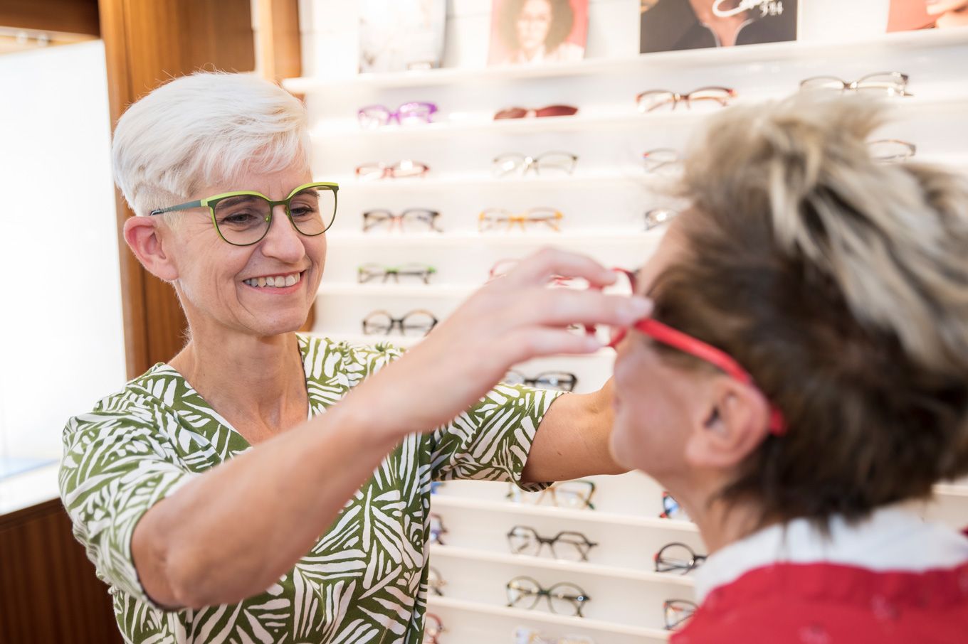 Foto: Innenansicht bei Optik NEMETZ Kontaktlinsen. Eine Dame mit Brille setzt einer Kundin eine Brille auf.